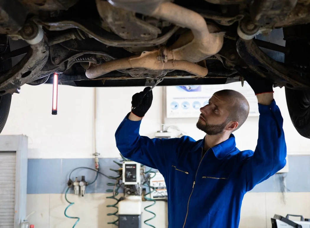 Mechaniker prüft die Abgasanlage unter dem Auto